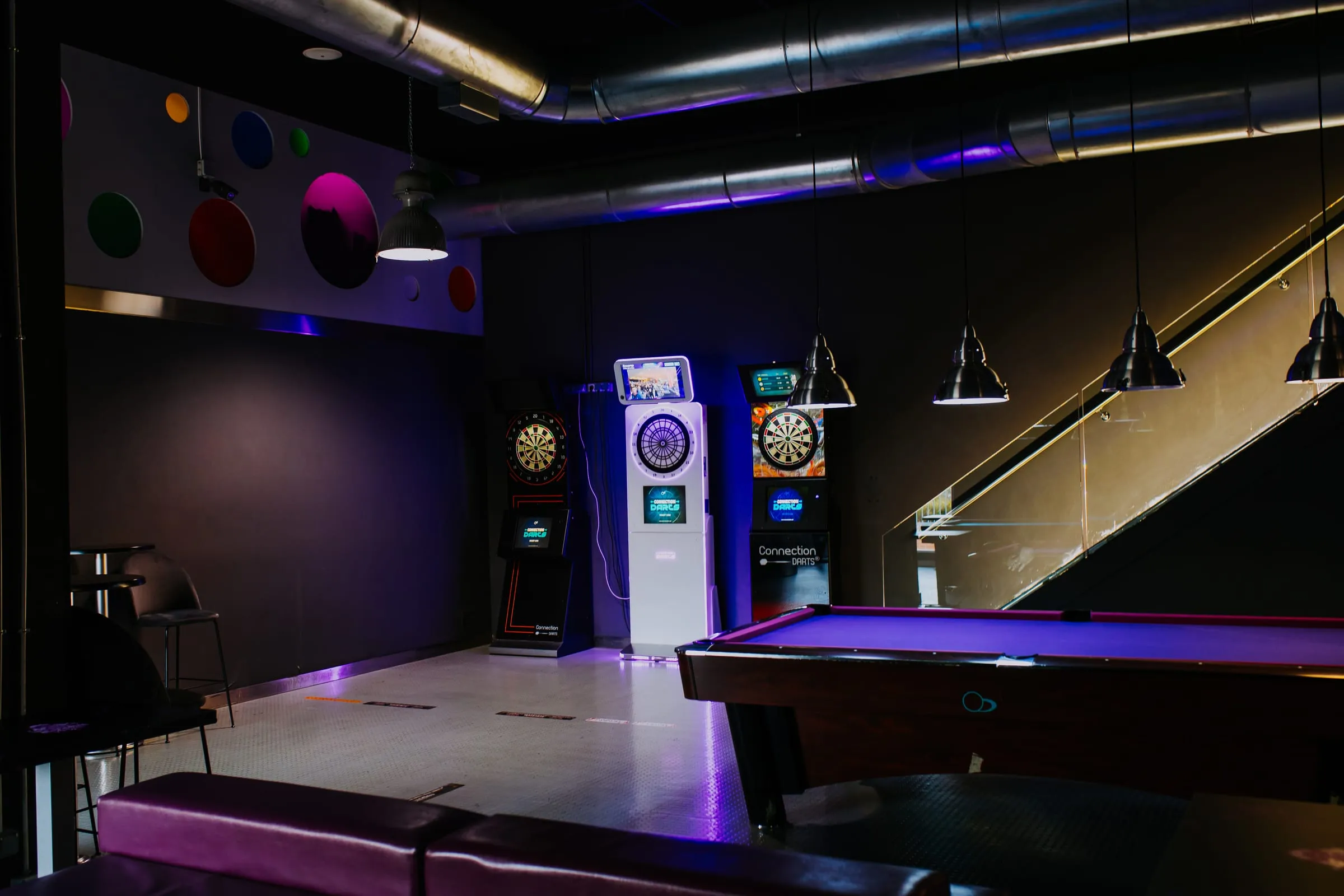 Sala de billar de Level 99 vacía, con las lámparas colgantes y las dianas encendidas.