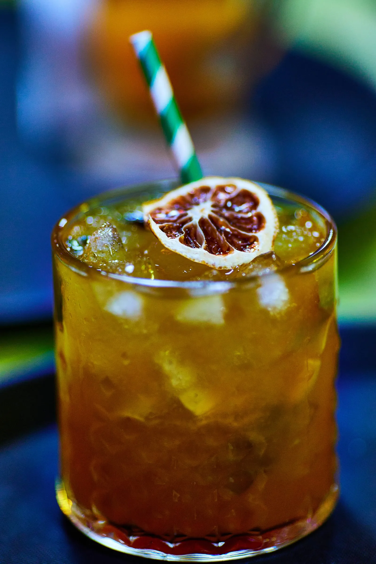 Cóctel con hielo y una rodaja de naranja seca, fotografiado a la altura del vaso.